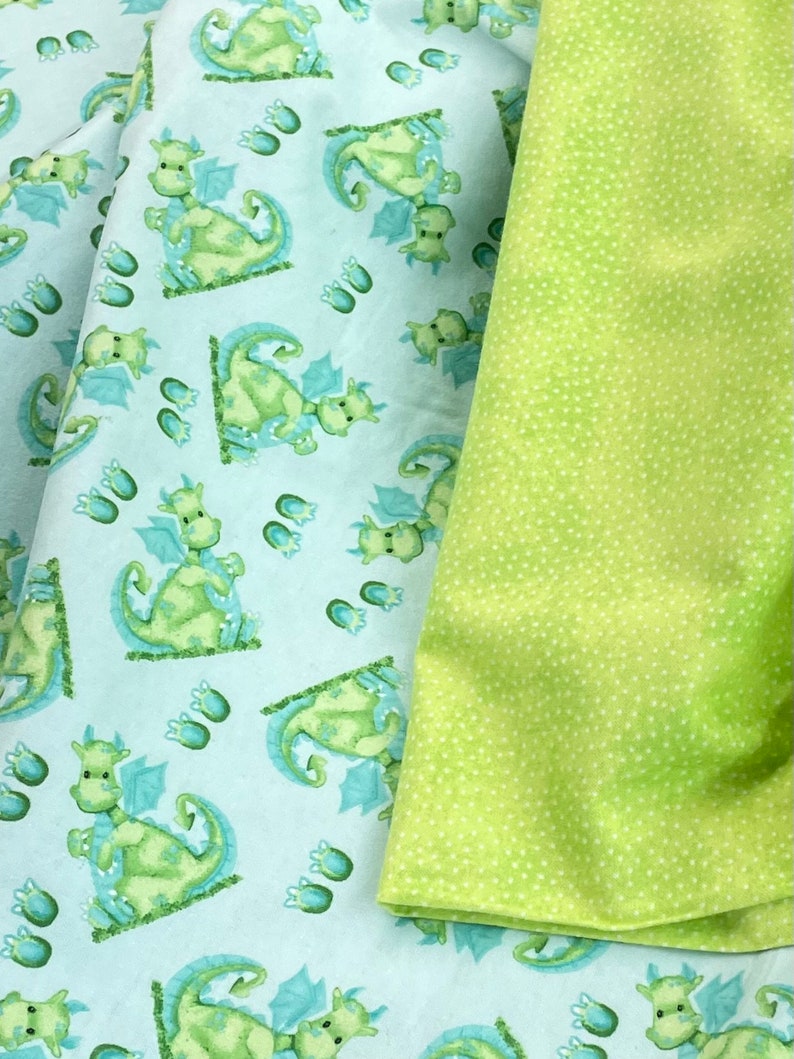 May include: Two pieces of fabric, one with a light blue background and a repeating pattern of green dragons, the other a solid green with white polka dots.