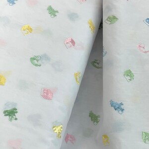 May include: White fabric with a repeating pattern of colourful embroidered toy blocks. The blocks are in shades of pink, yellow, green, and blue.