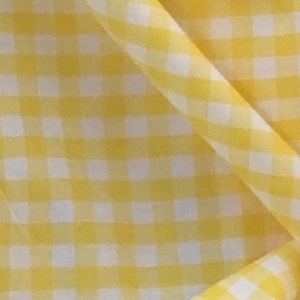 Może przedstawiać: Żółta i biała tkanina w kratę gingham z kratkowym wzorem. Tkanina jest złożona i ma miękką, gładką fakturę.