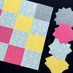 May include: A quilt top with a patchwork design featuring squares of yellow, pink, blue and grey fabric. The squares are decorated with different patterns, including stars, moons and cows. The quilt top is surrounded by a black background.