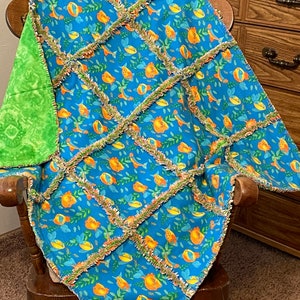 May include: A blue and green baby blanket with a fish and seaweed pattern. The blanket is made of soft, fluffy fabric and has a ruffled edge.