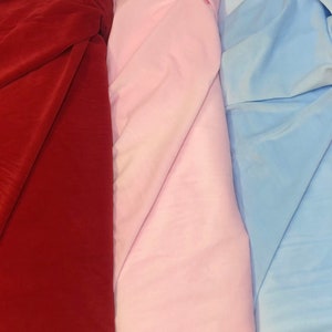 May include: Three fabric swatches, one red, one pink, and one light blue. The fabric is folded in thirds, with the folds running diagonally across the image.