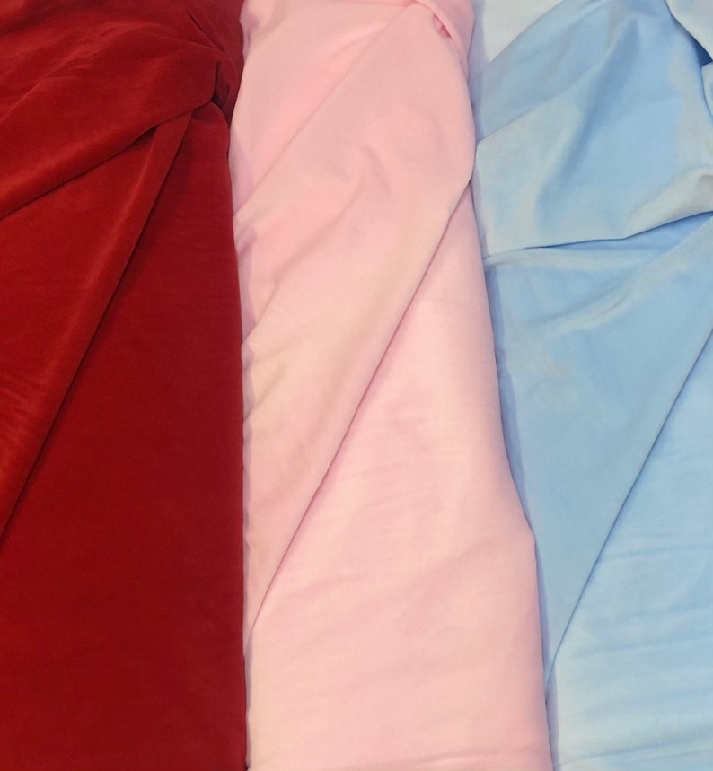 May include: Three fabric swatches, one red, one pink, and one light blue. The fabric is folded in thirds, with the folds running diagonally across the image.