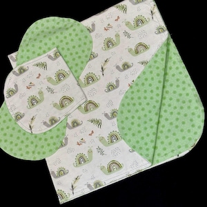 Könnte beinhalten: Ein Set aus Stoffartikeln, bestehend aus einem rechteckigen Tuch und einem kleineren abgerundeten Tuch, beide mit weißem Hintergrund und einem wiederkehrenden Muster aus hellgrünen Schnecken und kleinen braunen Farnen, akzentuiert durch hellgrünen Stoff mit weißen Punkten.