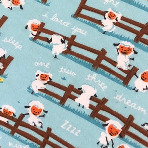 May include: A blue and brown fabric with a repeating pattern of white sheep jumping over a brown fence. The sheep have orange faces and the text "good night", "I love you", "sleep", "and two", "there dream", "Zzzz", and "night" is written on the fabric.