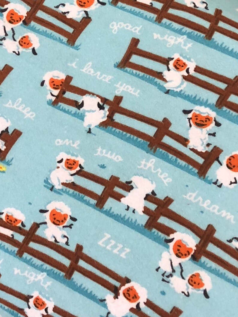 May include: A blue and brown fabric with a repeating pattern of white sheep jumping over a brown fence. The sheep have orange faces and the text "good night", "I love you", "sleep", "and two", "there dream", "Zzzz", and "night" is written on the fabric.