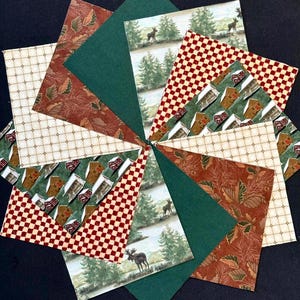 May include: A circular arrangement of paper pieces in various patterns and colours. The design includes green, red, and brown sections with images of cabins, deer, and foliage. The overall theme is rustic and nature-inspired.