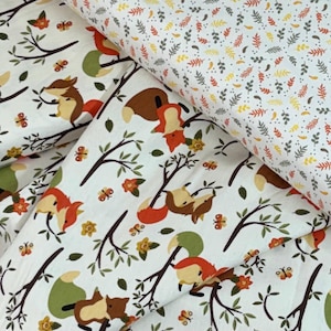 May include: White fabric with a repeating pattern of foxes, branches, flowers, and butterflies in brown, orange, and green. A second fabric features a pattern of small leaves in orange, yellow, and green.