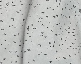 May include: A white fabric with a repeating pattern of black stars, moons, and diamonds. The fabric has a subtle texture.