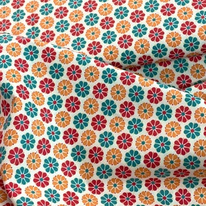 May include: Close-up of a white fabric with a repeating floral pattern. The flowers are in red, teal, and orange, arranged in a grid-like design. The fabric is slightly wrinkled, suggesting it's a textile.