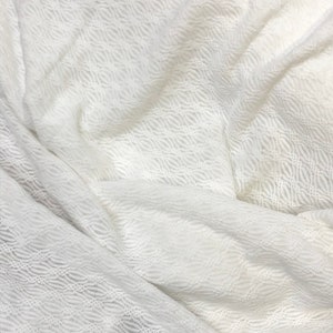 May include: White crochet fabric with a wavy pattern. The fabric is soft and delicate, and it has a slightly sheer appearance.