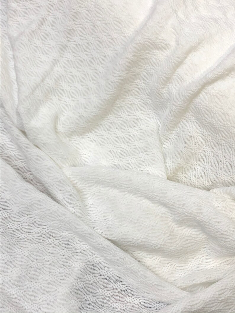 May include: White crochet fabric with a wavy pattern. The fabric is soft and delicate, and it has a slightly sheer appearance.