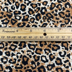 May include: Close-up of a brown and white fabric with a black leopard print pattern. A ruler is visible at the bottom of the image.