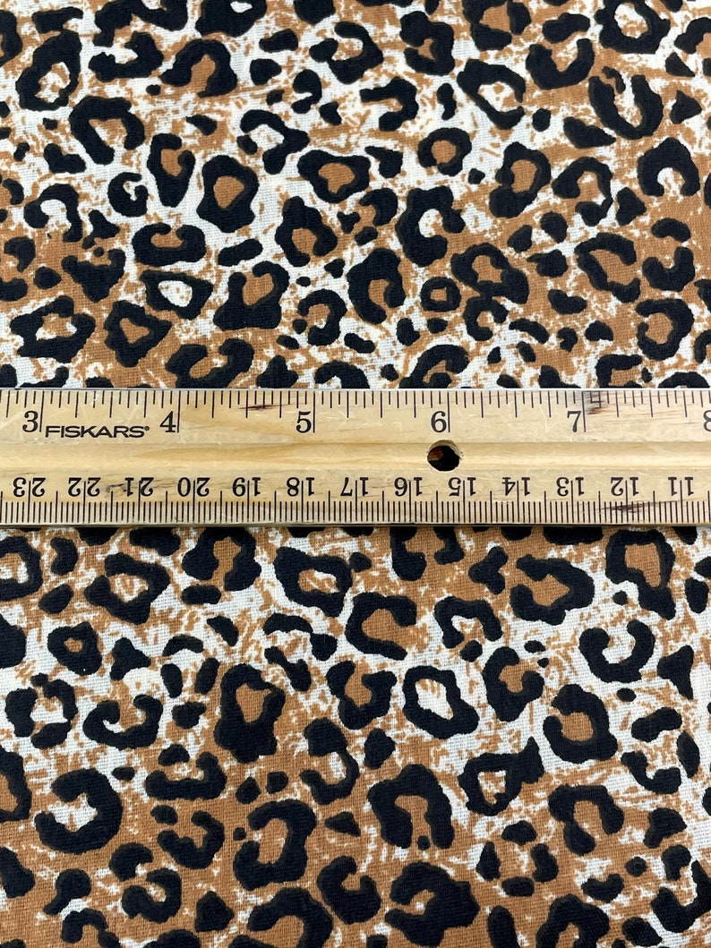 May include: Close-up of a brown and white fabric with a black leopard print pattern. A ruler is visible at the bottom of the image.