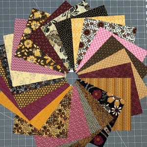 May include: A collection of square fabric swatches arranged in a circular fan pattern. The fabric pieces feature a variety of patterns including floral, geometric, and abstract designs in a color palette of mustard yellow, deep burgundy, black, and pink.
