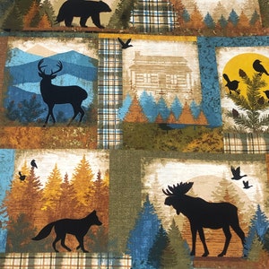 May include: A fabric with a patchwork design featuring woodland scenes. Silhouettes of a bear, deer, fox, and moose are set against backgrounds of mountains, cabins, and trees. The color palette includes shades of brown, blue, and green.