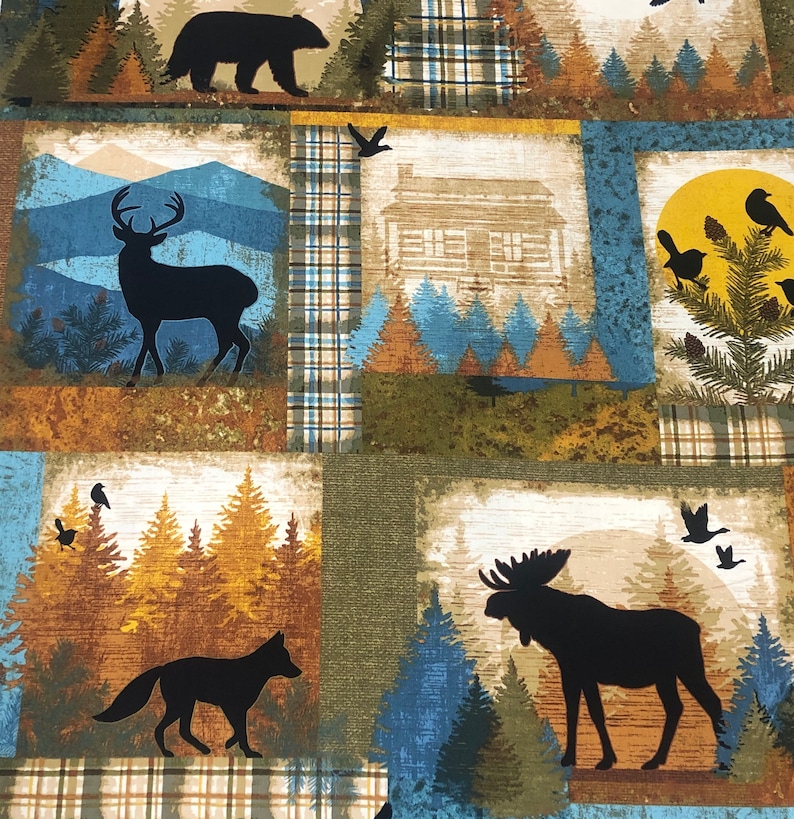 May include: A fabric with a patchwork design featuring woodland scenes. Silhouettes of a bear, deer, fox, and moose are set against backgrounds of mountains, cabins, and trees. The color palette includes shades of brown, blue, and green.