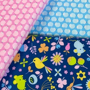May include: Three fabric swatches with different patterns. The first is pink with a repeating pattern of white hedgehogs. The second is light blue with a repeating pattern of white hedgehogs. The third is dark blue with a repeating pattern of yellow birds, green mice, pink flowers, and green leaves.