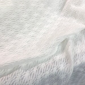 May include: White crochet fabric with a delicate, repeating pattern of ovals. The fabric is soft and sheer, with a slightly textured surface.