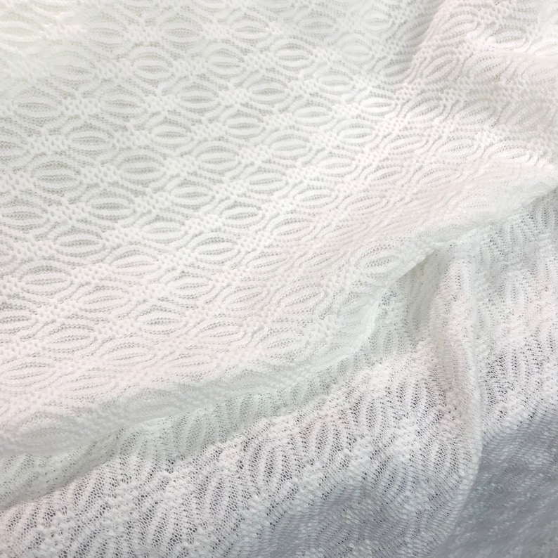 May include: White crochet fabric with a delicate, repeating pattern of ovals. The fabric is soft and sheer, with a slightly textured surface.
