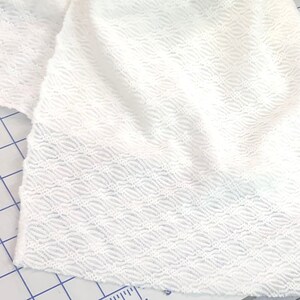 May include: White fabric with a textured, wavy pattern. The fabric is soft and has a slightly sheer appearance.