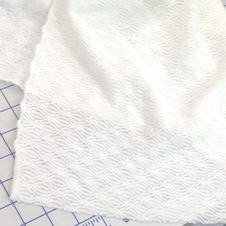 May include: White fabric with a textured, wavy pattern. The fabric is soft and has a slightly sheer appearance.