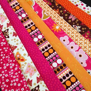 May include: A collection of fabric strips in various patterns and colors, including pink, orange, brown, and white. The strips feature floral, geometric, and butterfly designs.