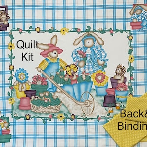 Op de afbeelding: Quiltset met een blauw-wit geruite achtergrond en een bloemige rand. In het midden van de afbeelding zijn twee konijnen te zien, één duwt een kruiwagen vol bloemen en de ander houdt een boeket bloemen vast. De tekst "Quilt Kit" staat op een wit banner.