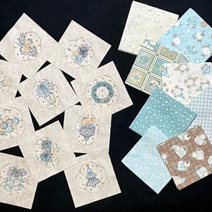 May include: A collection of 14 fabric squares with various winter holiday designs. The squares are in shades of blue, white, and brown. Some of the designs include snowflakes, ornaments, and a snowman.