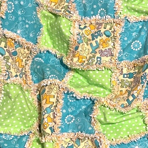 May include: A patchwork baby quilt with a green and blue color scheme. The quilt is made of squares of fabric with different animal prints, including deer, foxes, and birds. The squares are sewn together with a ruffled trim.