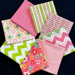 May include: A collection of eight pink and green fabric squares with various patterns, including floral, polka dots, stripes, and zigzags.