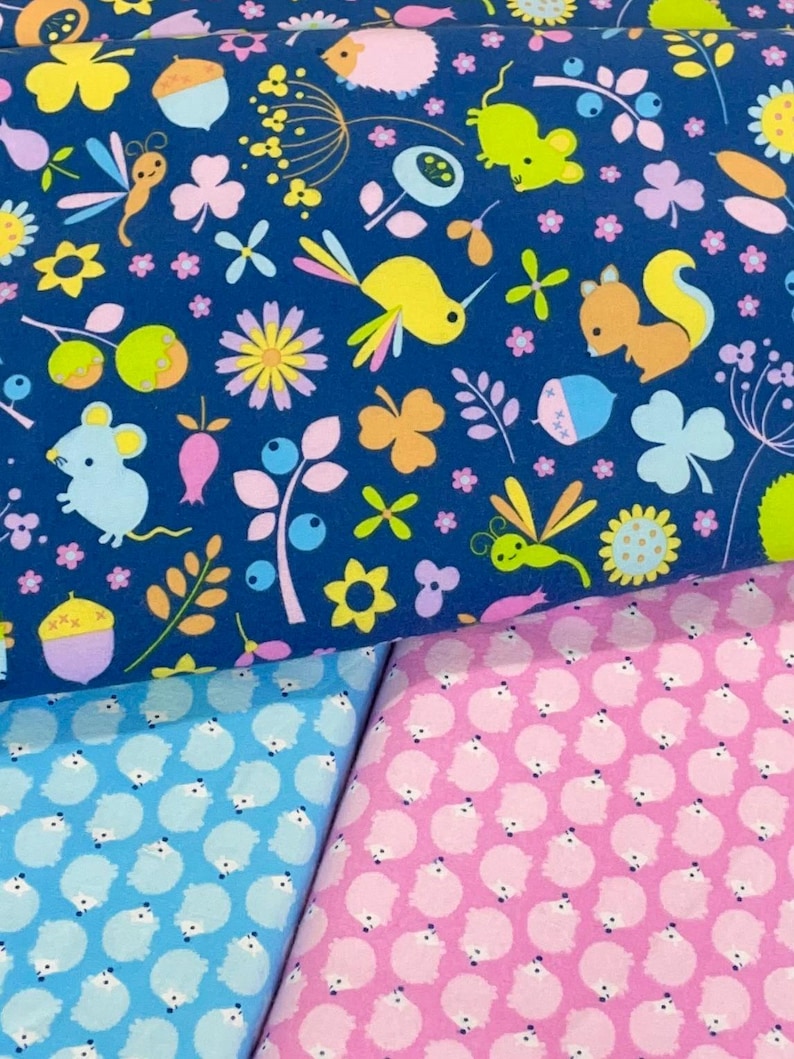 May include: Three fabric swatches with different patterns. The top swatch is a dark blue fabric with a repeating pattern of small animals, flowers, and leaves. The middle swatch is a light blue fabric with a repeating pattern of small white animals. The bottom swatch is a pink fabric with a repeating pattern of small white animals.