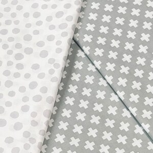 Puede incluir: Dos muestras de tela, una con fondo blanco y lunares grises, la otra con fondo gris y signos m&aacute;s blancos.