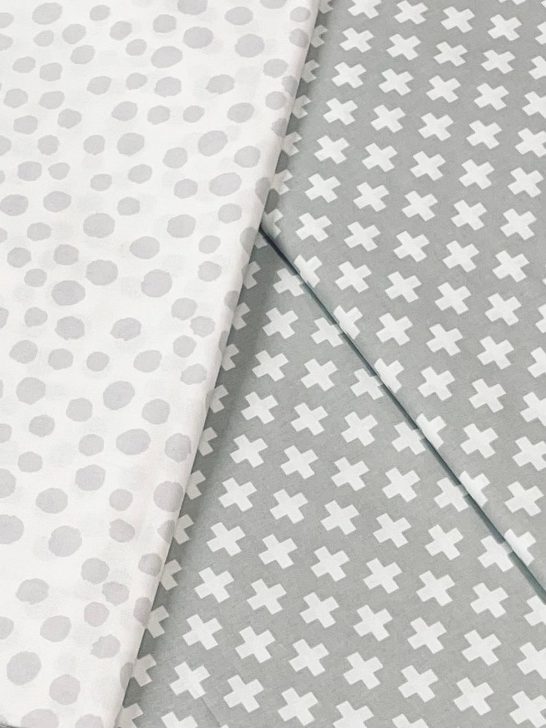 Puede incluir: Dos muestras de tela, una con fondo blanco y lunares grises, la otra con fondo gris y signos m&aacute;s blancos.