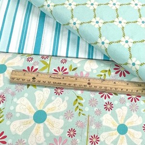 May include: A close-up of three different fabric swatches. The top swatch is a light blue fabric with a white and green floral pattern. The middle swatch is a white fabric with blue stripes. The bottom swatch is a light blue fabric with a white floral pattern and a red accent.