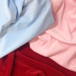 May include: A close-up of three fabric swatches. The swatches are a light blue, a pink, and a deep red.