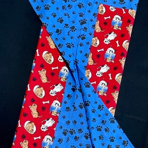 May include: A red and blue fabric blanket with a paw print pattern on one side and a pattern of dogs reading books on the other side.