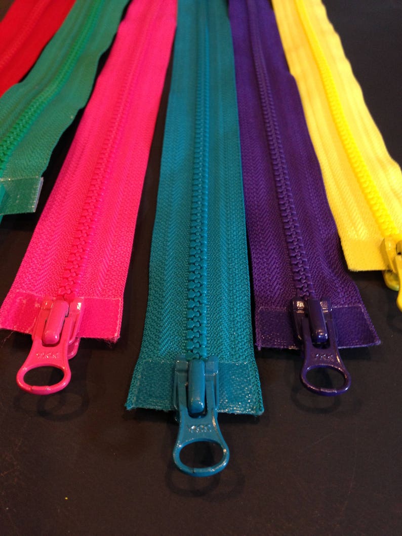 May include: Assortment of colorful zipper tapes with metal sliders. The zippers are in the colors red, green, pink, teal, purple, and yellow.