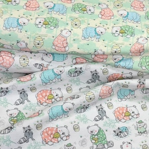May include: White fabric with a repeating pattern of bears wearing pyjamas. The bears are in various poses, including sleeping, sitting, and standing. The fabric also features honeycombs, raccoons, and leaves.
