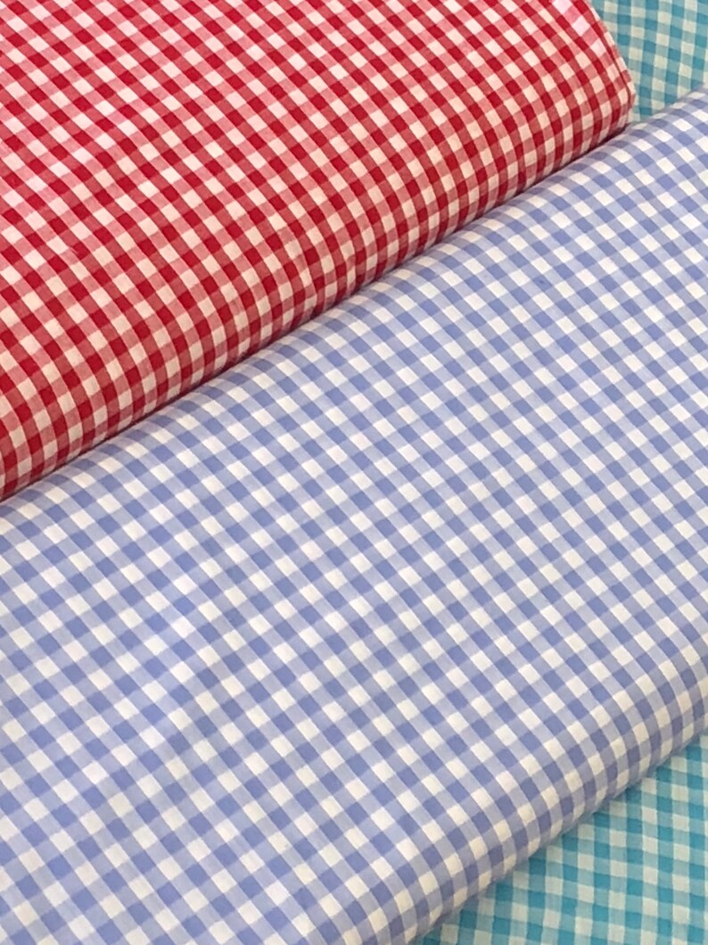 May include: Three rolls of gingham fabric in red, blue, and turquoise. The fabric has a checkered pattern.
