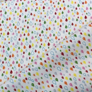 May include: White fabric featuring a repeating pattern of colourful teardrop shapes in shades of red, orange, yellow, green, pink, and grey. The teardrops are outlined in blue. The fabric is folded, showing the pattern at different angles.