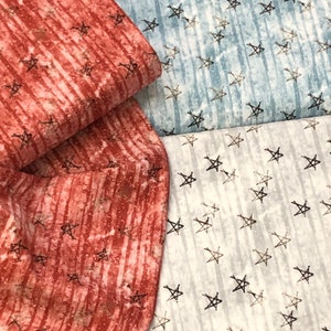 May include: Two fabric swatches with a star pattern. The top swatch is a light blue with white stars. The bottom swatch is a red and white striped fabric with white stars.