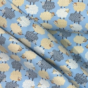 May include: Light blue fabric with a repeating pattern of sheep in various colors, including white, tan, and gray. The sheep are arranged in a scattered layout across the fabric, creating a whimsical and playful design. The fabric has a soft, slightly wrinkled appearance.