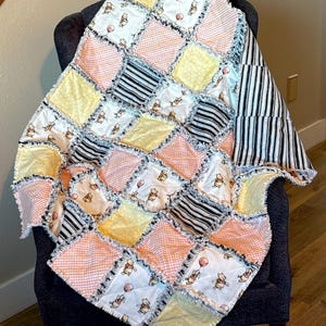 May include: A rag quilt featuring a patchwork design of squares in various patterns including a white fabric with Winnie the Pooh characters, yellow polka dots, peach gingham, and black and white stripes, all joined with frayed exposed seams.