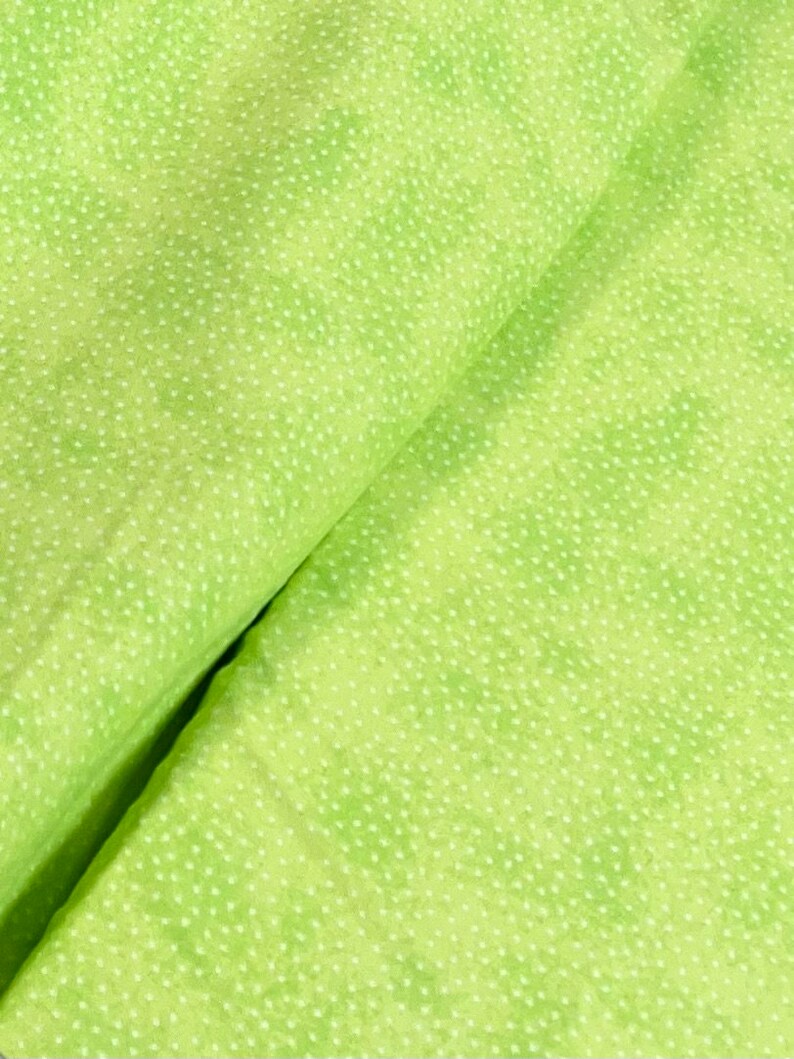 May include: A close-up of a green fabric with a white polka dot pattern. The fabric is folded in half, showing the pattern on both sides.