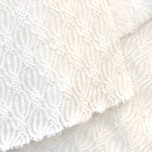 May include: White crocheted fabric with a textured pattern. The fabric is soft and delicate, and it has a slightly frayed edge.