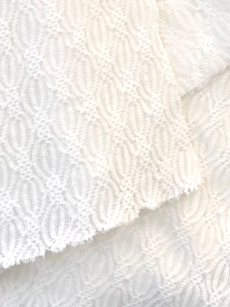 May include: White crocheted fabric with a textured pattern. The fabric is soft and delicate, and it has a slightly frayed edge.