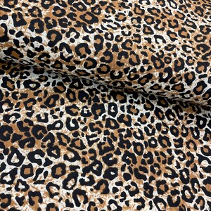 May include: Brown, black, and white leopard print fabric. The fabric has a textured surface.