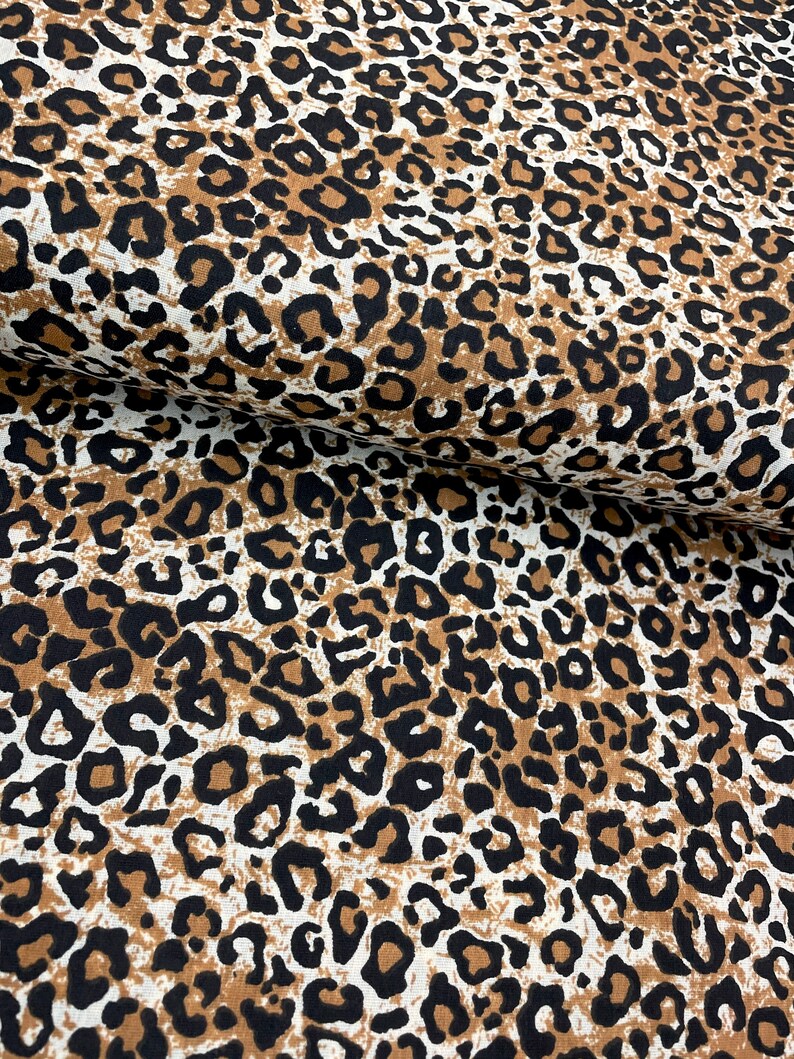May include: Brown, black, and white leopard print fabric. The fabric has a textured surface.