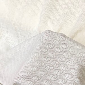 May include: White textured fabric with a woven pattern. The fabric is folded in half, showing the texture and pattern on both sides.